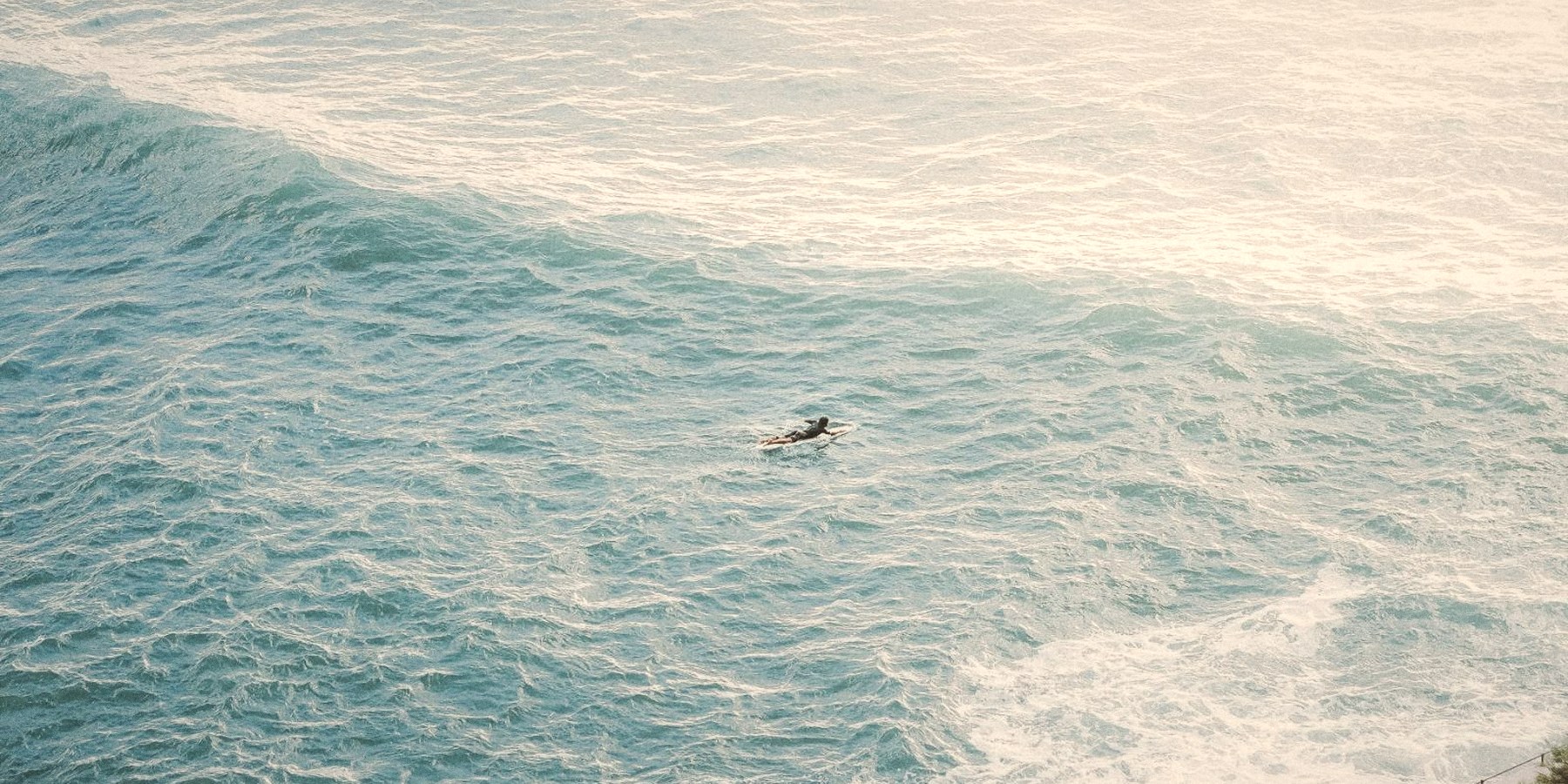A surfer paddling through the waves, seen from above, in Biarritz