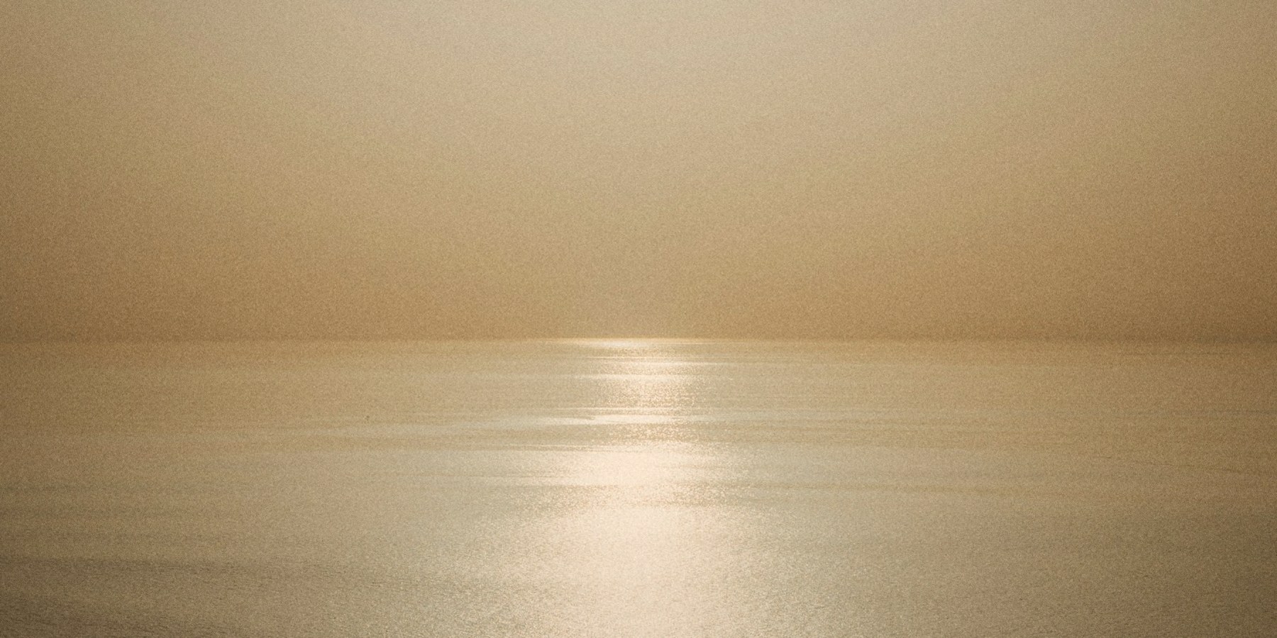 Low sun over the ocean in Biarritz, surfers on the horizon