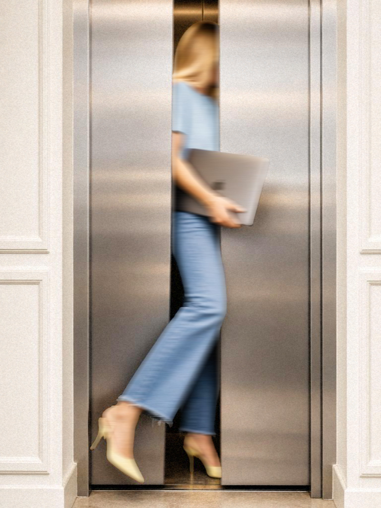 A woman in a hurry, laptop under her arm, stepping out of a lift