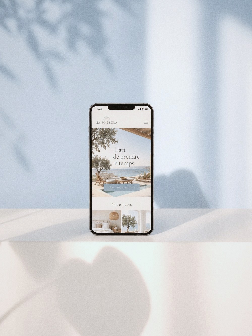 A phone showing a holiday-home website, against a blue wall with leaf shadows